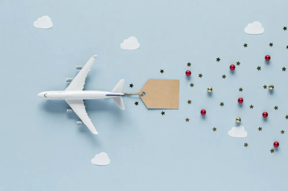 A toy plane on a blue backdrop attached to a tag with small Christmas ornaments trailing behind it